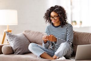 Woman sitting with her legs crossed on her couch using her free phone and internet she got through the Federal Affordable Connectivity Program